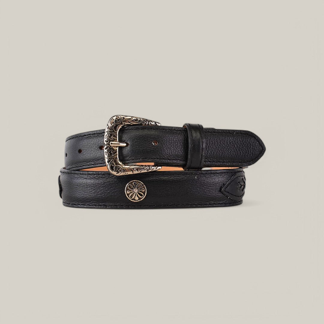The Alexa Black Belt - Roller Buckle features a black leather design with an intricate gold buckle and an engraved floral motif, perfect for womens collections. Coiled on a beige background, it highlights its texture and elegance as a must-have wardrobe accessory.