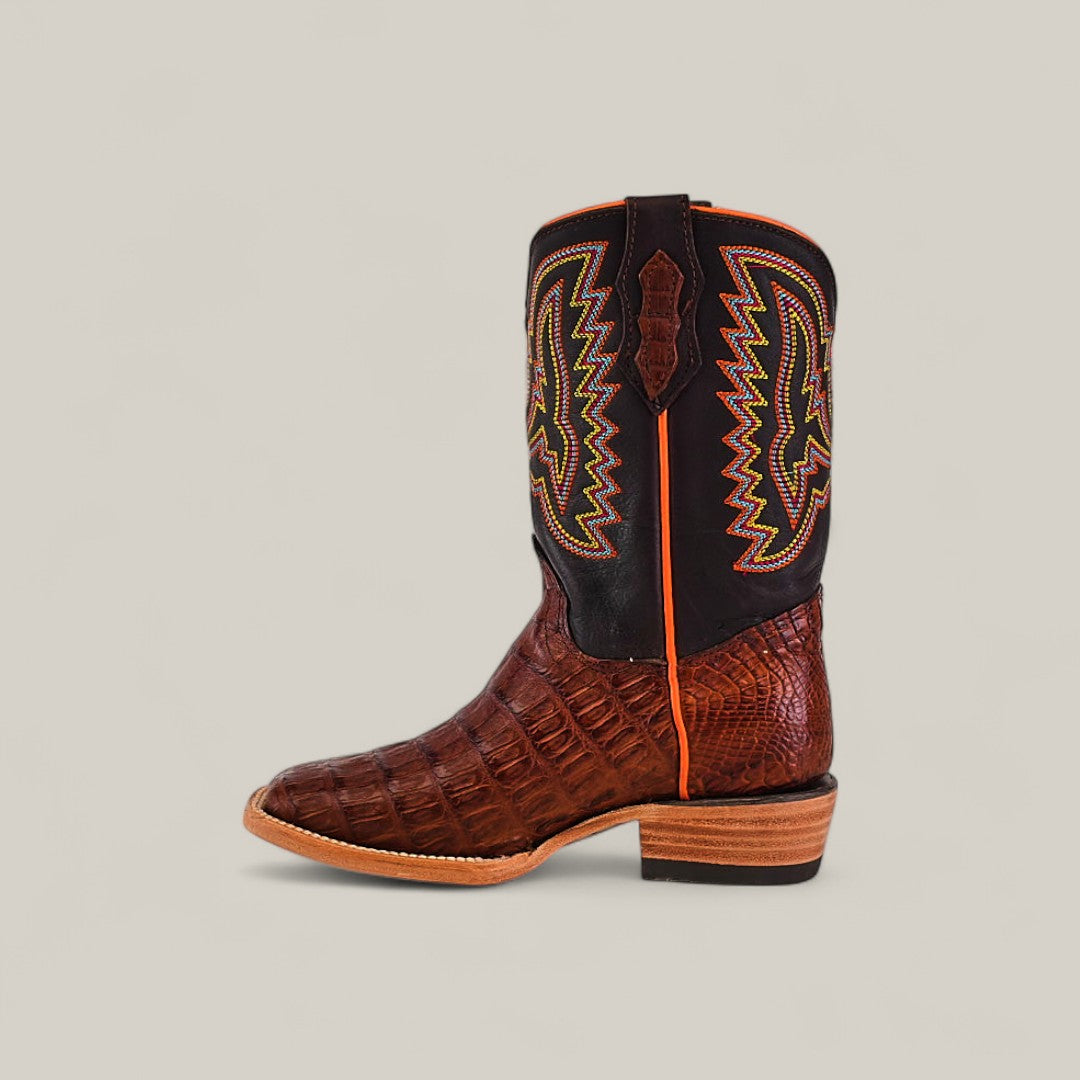The Exotic Caiman Belly Tail Cognac Kids Boots feature a square toe, brown textured leather foot, stacked heel, and a black shaft with yellow, green, and orange zigzag stitching on a neutral background.