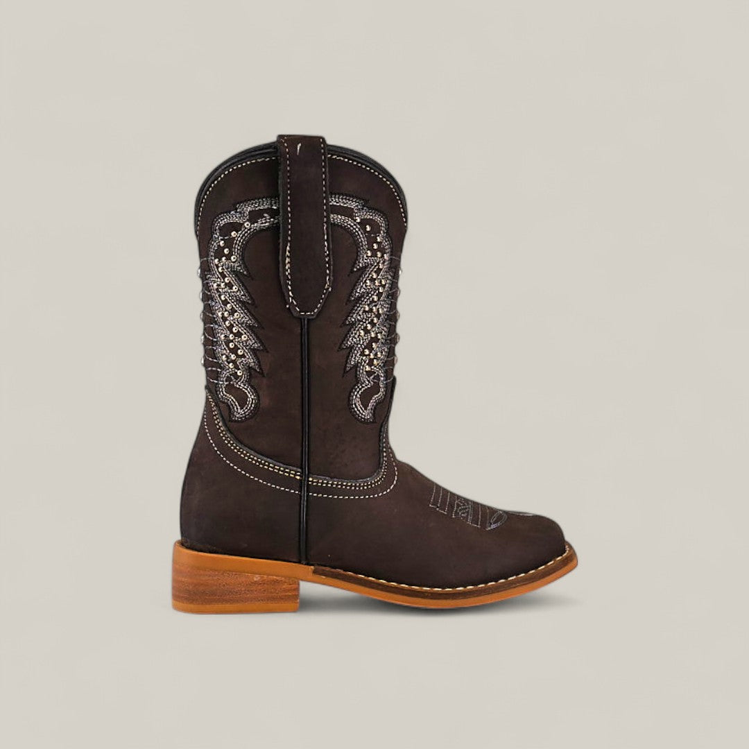 The Orion Suede Oxford - Square Toe Kids Boot is shown in profile, featuring dark brown suede, decorative white stitching, a rounded toe, and a light tan stacked heel against a plain light background.