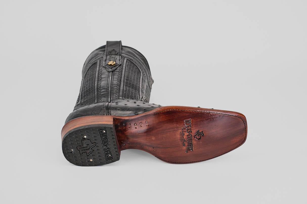 The Exotic Ostrich - Black boot with a narrow square toe lies on its side, showing detailed stitching on the upper and a wooden sole engraved with the “Los Altos Boots” logo.