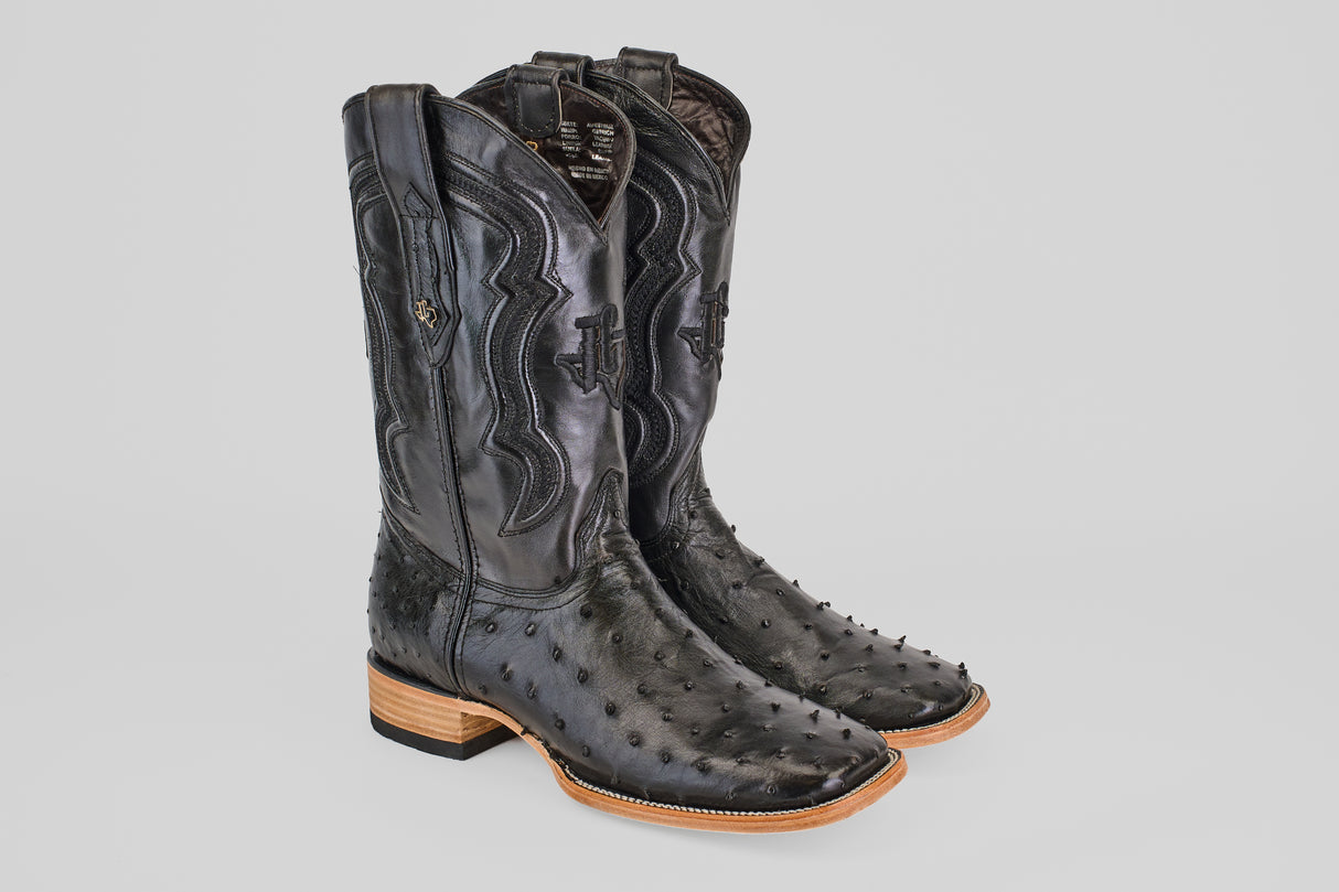 The Austin - Black - Square Toe boots feature decorative stitching, square toes, and light brown stacked heels, crafted in black avestruz leather and displayed against a plain light gray background.