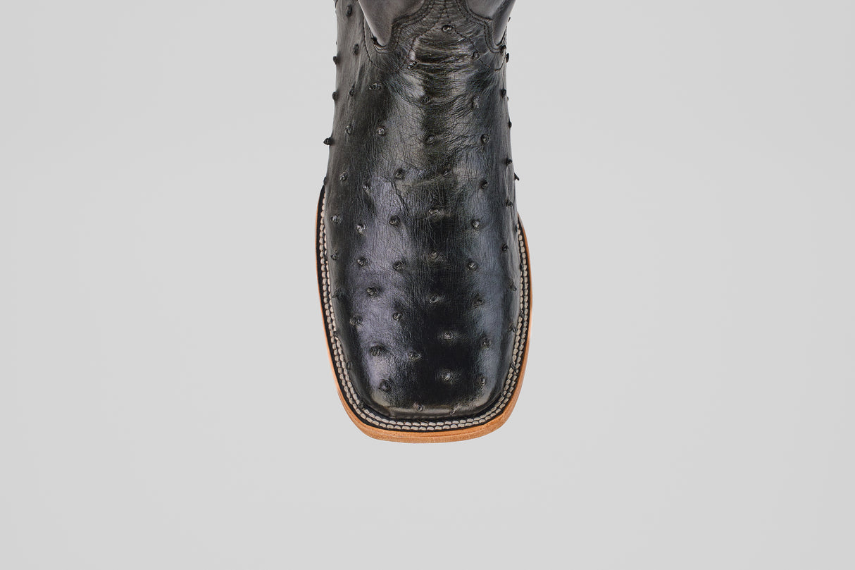 A close-up of the Austin - Black - Square Toe cowboy boot showcases its black avestruz leather, square toe, textured surface, and visible stitching along the light brown sole against a plain light background. Model: AV20 Negro.