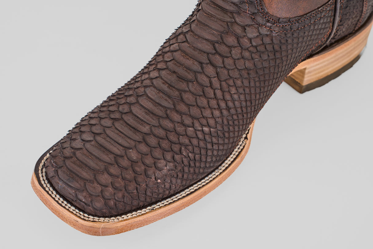 Close-up of the Tanner - Matte Brown - Square Toe boot, featuring a textured, scale-like leather pattern, light-colored stitching along the edge, and a light wooden sole.