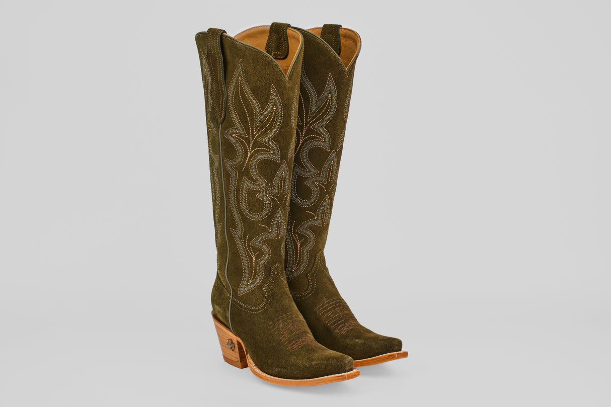 A pair of Allison Agave - Tall Shaft - Snip Toe women’s cowboy boots in dark green suede with tan stitching, pointed toes, and light brown stacked heels are standing upright against a light gray background.
