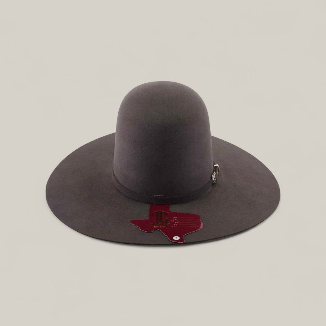 The 10X - Oxford - TC Hats is a wide-brimmed, dark Western hat with a tall, shapeable open crown. It’s displayed on a plain light background and features a red Texas-shaped tag on the brim with small text and graphics.