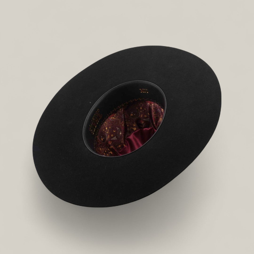 A 10X - Black - TC Hats open crown Texana hat is showcased upside down, displaying its maroon paisley satin lining against a plain light beige background.