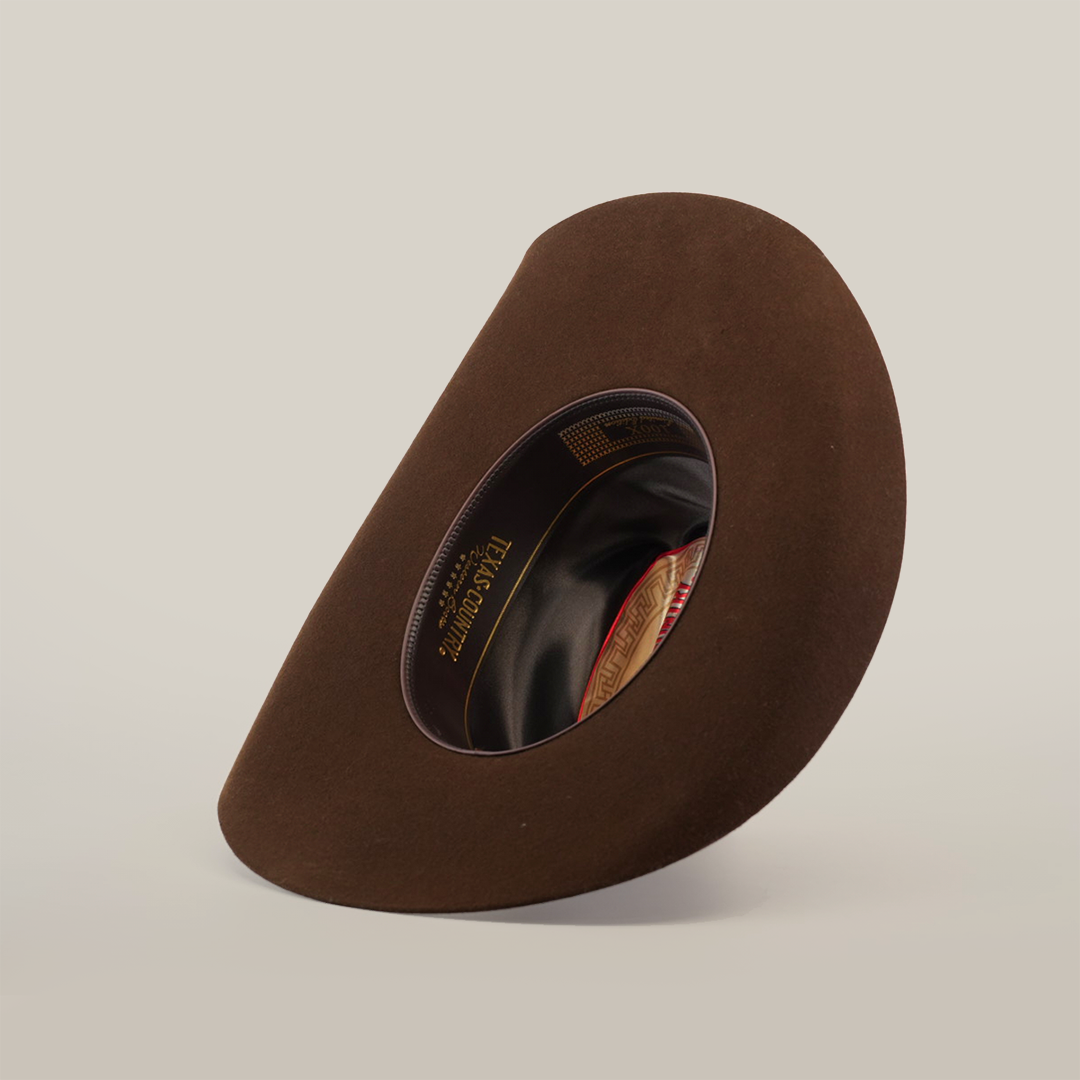The 6X Dallas Brown felt hat is displayed on its side, highlighting its Western sophistication with visible interior lining and branding. Its distinctive shape and rich color stand out against the plain white background, making it ideal for those seeking classic cowboy charm.