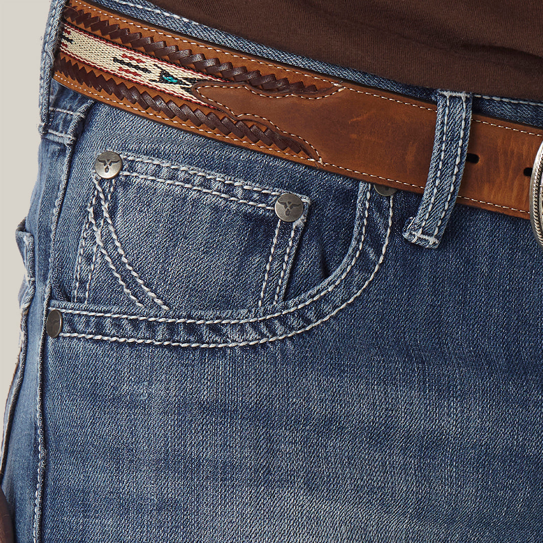 Close-up of a person wearing Mens Wrangler 20X No. 42 Vintage Bootcut Jeans - 1042MWXLB in premium denim with detailed stitching, paired with a decorative brown leather belt and partially visible metal buckle against a light, neutral background.