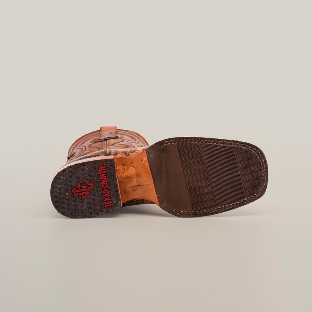 Close-up of the Handtooled Leave Orix cowboy boots sole shows detailed stitching and a slip-resistant rubber heel. The red Texas Country imprint appears with a textured grip pattern. Made from premium cowhide leather, this boot also boasts decorative stitching on the upper part.