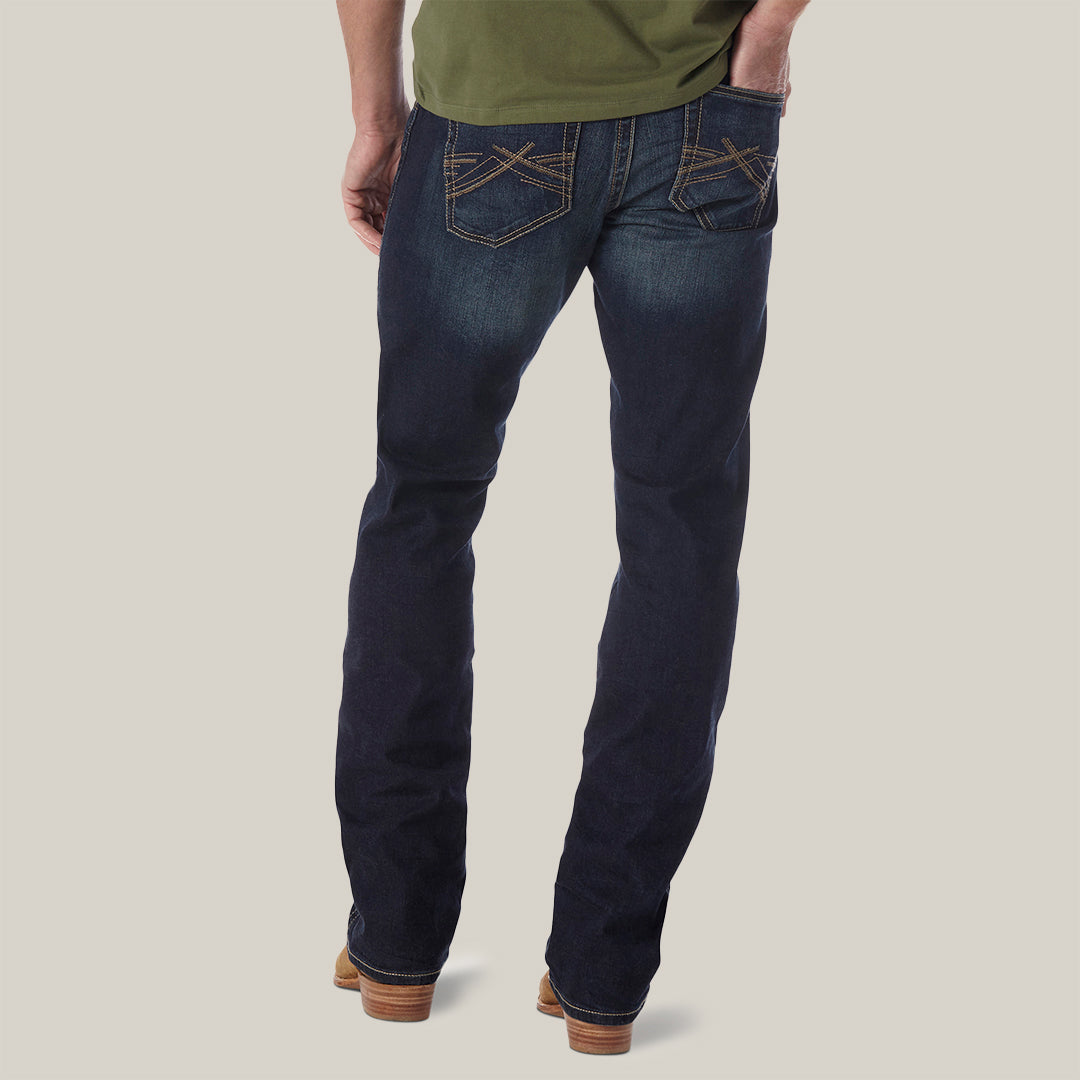 A person is shown from the back wearing Mens Wrangler 20X No. 42 Vintage Bootcut Jeans (42MWXRD) with decorative stitching on the back pockets, paired with a green shirt and brown shoes against a plain background.