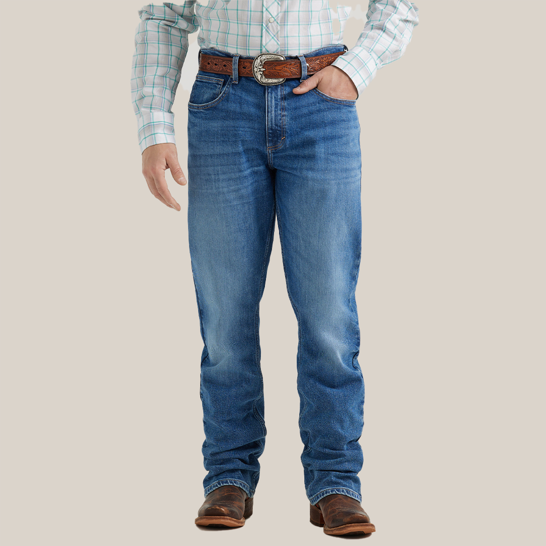 A person stands facing away wearing Wrangler 20x Mens Medium Wash Backwater Vintage Bootcut Stretch Denim Jeans with decorative stitching, a plaid shirt, and brown leather sandals against a light gray background.