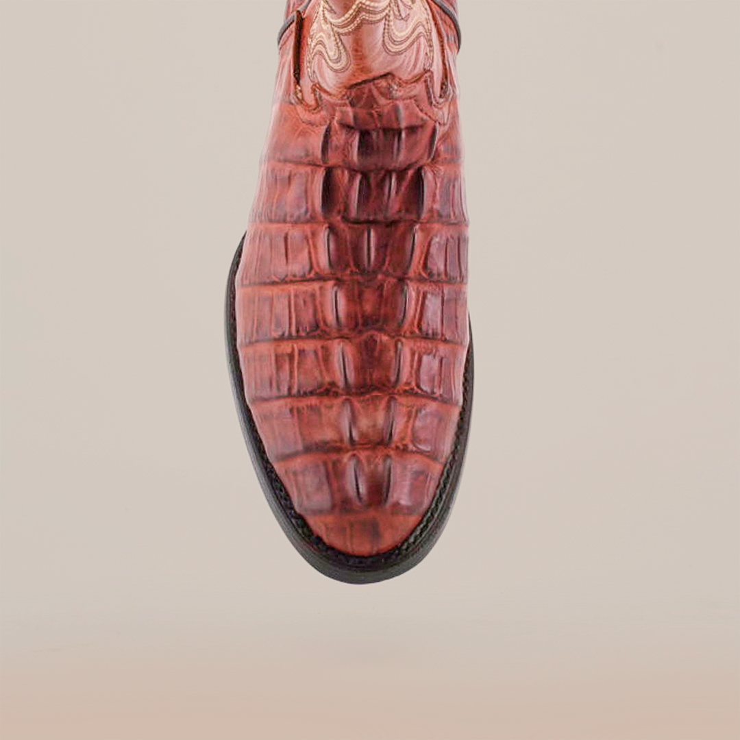 The Crocodile Tail Print Cogñac boot features a brown crocodile tail print on the front, intricate upper stitching for a decorative flair, and a premium dark leather sole that contrasts with the lighter upper. The plain light background highlights the boots unique details.