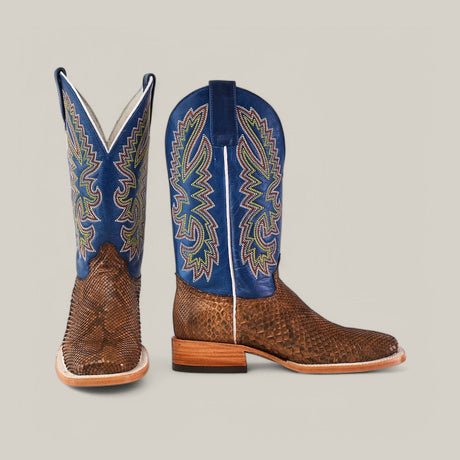 A pair of cowboy boots with brown textured leather on the foot and blue uppers featuring colorful, intricate stitching, displayed against a light gray background.