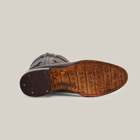 The image displays the sole of a Rush Brown - Roper Toe boot, made from premium cowhide leather. The textured leather sole mimics crocodile skin, showcasing visible stitching and metal studs by the heel, set against a white background.