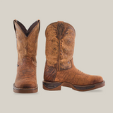 A pair of handcrafted Tan Brown Rough Out boots, with one facing forward and the other turned sideways, display intricate stitching on premium waterproof cowhide leather. They feature composite toes, dark soles, and a rugged, worn texture.