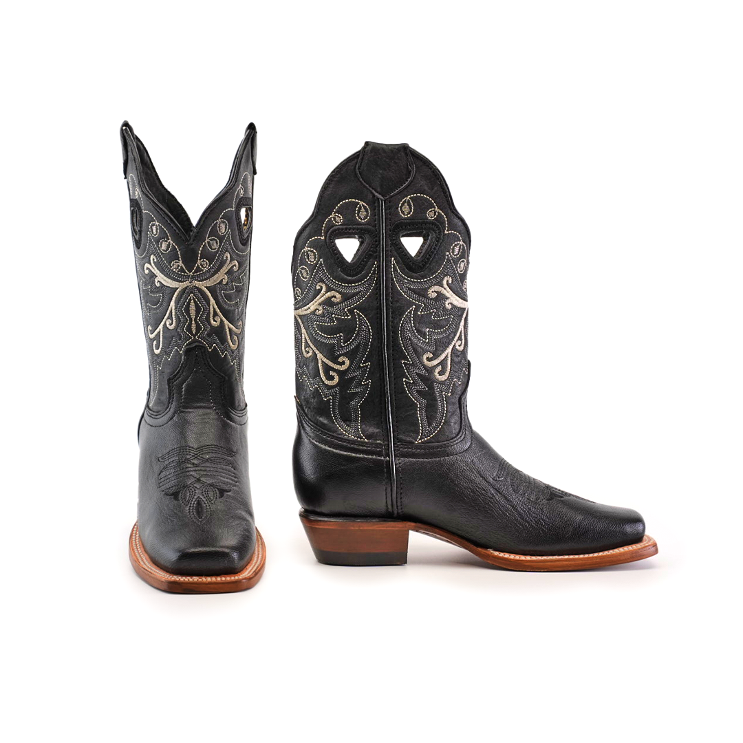 The Western Stitch Black Lustre boots feature ornate silver stitching, showcasing traditional craftsmanship. With narrow square toes and brown leather soles, one boot stands upright while the other is tilted to highlight its intricate side pattern.