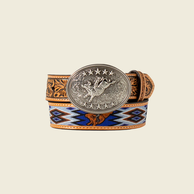 The 3D Youth Boys Bullrider Canvas Belt D120003927 showcases a western-inspired design, featuring an intricately engraved strap with floral and colorful geometric patterns, and a large oval silver buckle displaying a cowboy on a bucking bronco motif surrounded by stars.