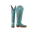 A pair of Brittany Rustic Ceramic Tall Shaft Snip Toe Boots in turquoise features intricate swirling embroidery, brown wooden heels, and a genuine leather sole. One boot stands upright while the other tilts, showing off the side zipper and pointed toe design.