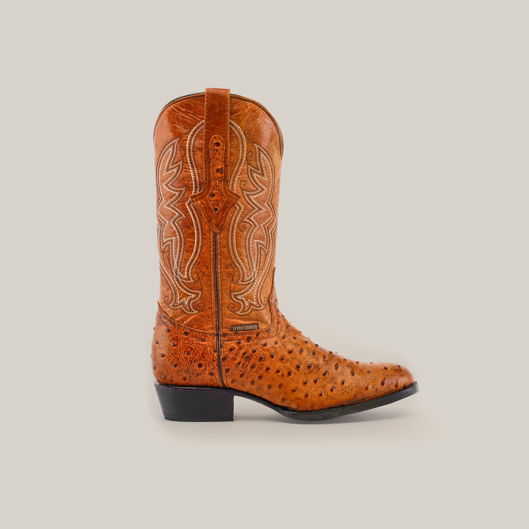 The Karoo Ostrich Print Buttercup - Round Toe boot features brown leather with intricate white stitching and a sleek ostrich print. It includes a low heel, leather sole, and a pull strap, all presented elegantly against a white background.