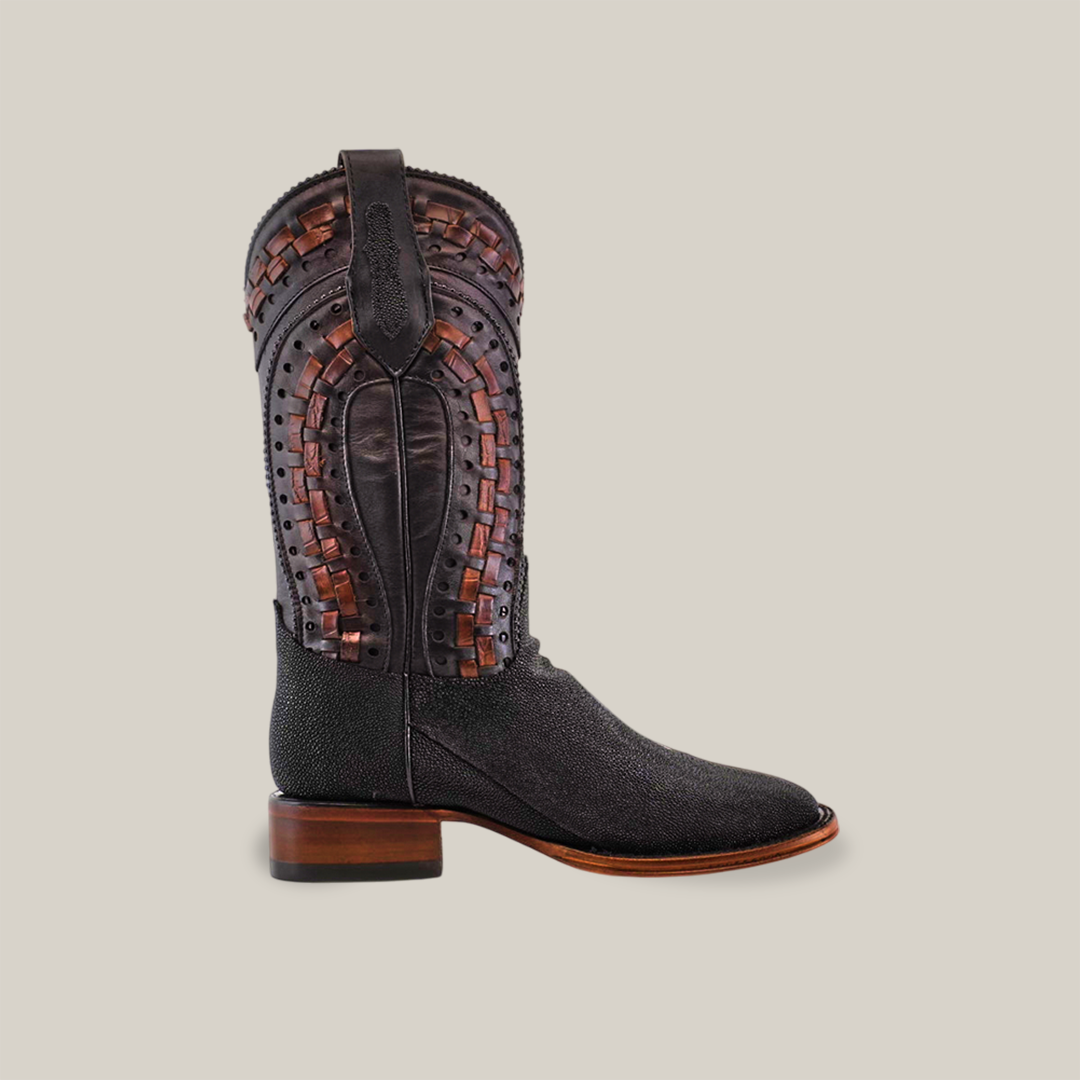 The Exotic Stingray - Herradura boot in black epitomizes exquisite craftsmanship with brown woven leather details on the upper shaft. It features a square toe, Goodyear welt sole, and wooden heel, showcased elegantly against a white background.