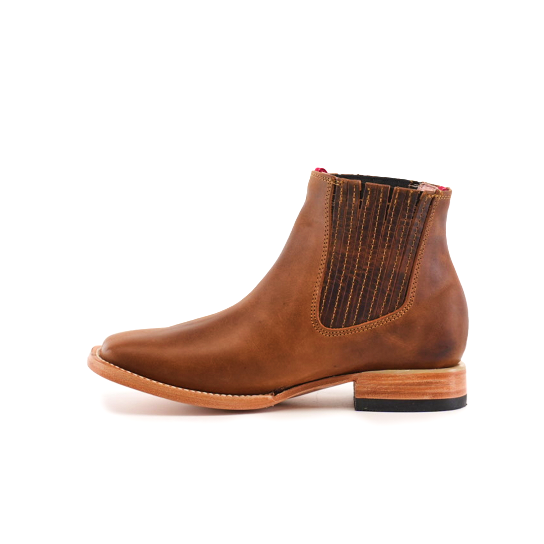 The Avejentado Honey Square Toe ankle boot in brown leather has an elastic side panel and wooden sole. Its polished finish and low heel add a subtle cowboy flair, making it a standout piece.