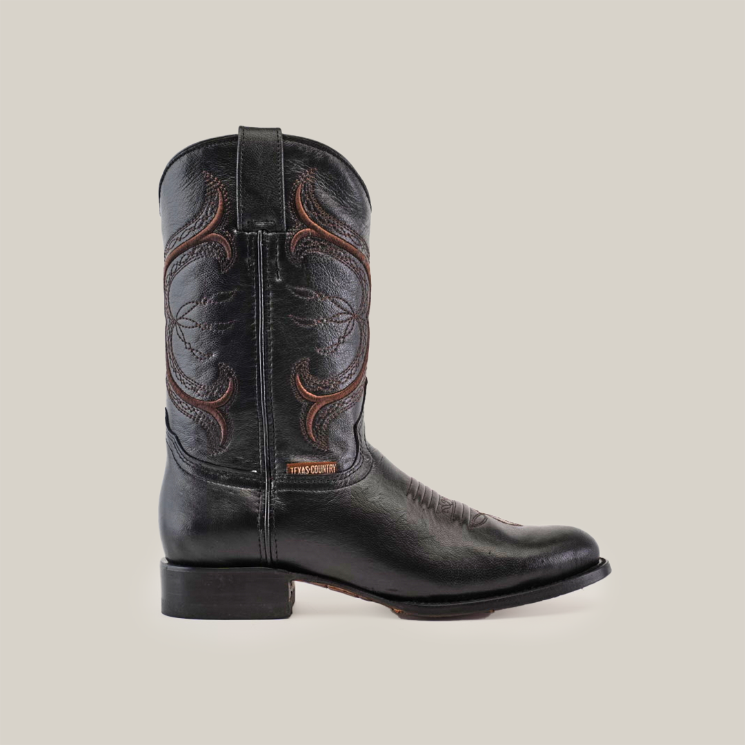 The Rush Black - Roper Toe boot captures the Western essence with its detailed brown stitching on premium cowhide leather. It features a low heel and a pull tab, set against a simple white background to highlight its black leather craftsmanship.