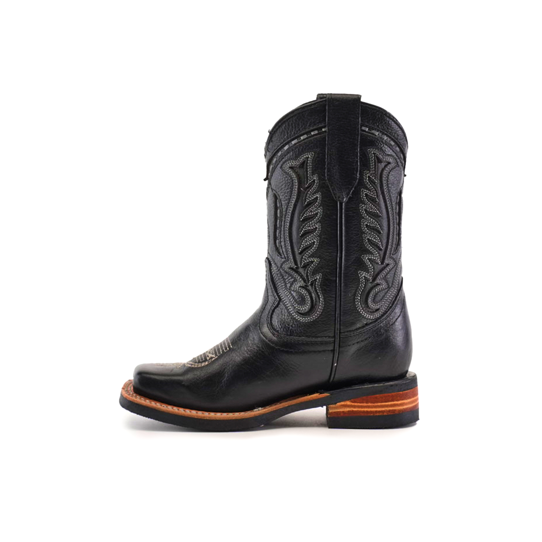 The Barcelona Black Lustre Rodeo Toe boot, made from premium cowhide leather, boasts intricate stitching with a brown stacked heel. This black boot has a wide square toe and pull tabs, all highlighted against a white background.