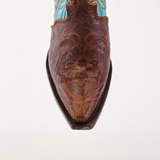 A close-up of the Premier Tabaco Handtooled Flowers boot reveals intricate brown leather floral tooling and stitching on the snip toe, contrasted by a blue leather tall shaft, highlighting its Western elegance.