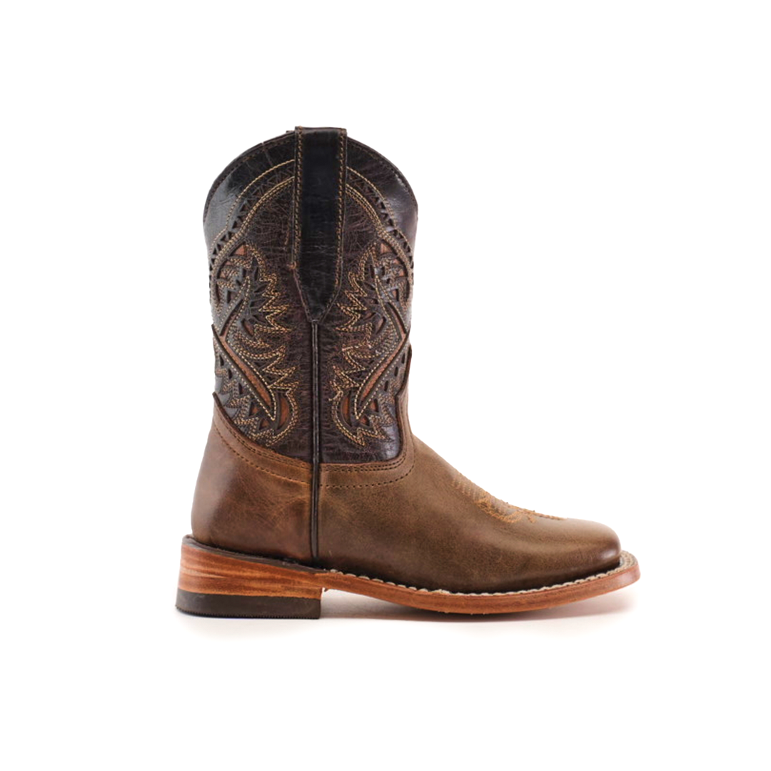 The Ranch Camel Square Toe is a brown leather cowboy boot, showcasing western elegance with intricate stitching and a slightly raised heel. Crafted from premium cowhide, it features a darker shaft adorned with decorative patterns, viewed stylishly from the side.