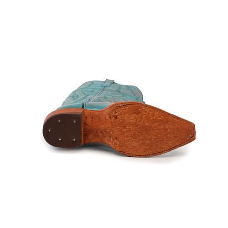 A turquoise cowboy boot lies on its side, showcasing a rich brown wooden sole with intricate carvings. This handcrafted boot has a dark brown heel with metallic studs and an embossed upper, echoing the style of the Brittany Rustic Ceramic Tall Shaft Snip Toe Boot.