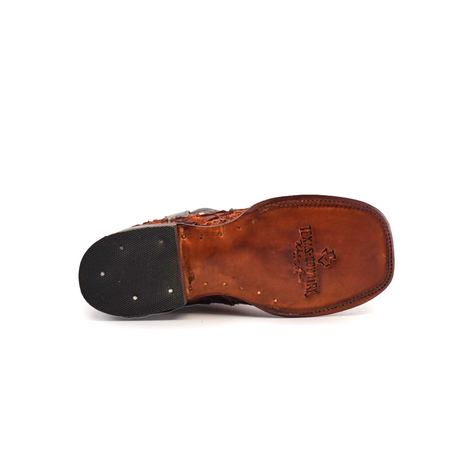 The bottom view of the Exotic Pirarucu Fish Patchwork Cogñac Square Toe shoe showcases a branded logo and text on the sole. The heel includes a rubber section with metallic nail heads. A scuffed appearance adds rugged charm to its worn sole, reminiscent of brown leather square toe boots.