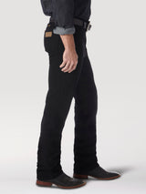 Side view of a person in Wrangler Cowboy Cut Slim Fit Jean - 0936WBK with a brown leather patch, black belt, and dark shirt with rolled sleeves. Complemented by black boots, the outfit stands out against a plain light background, highlighting the premium denim style.