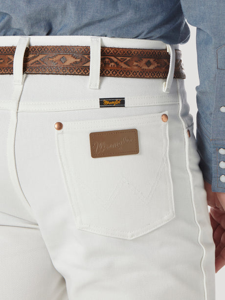 A person wears Wrangler Cowboy Cut Slim Fit White Jeans - 0936WHI, complemented by a brown leather belt. The jeans feature a Wrangler patch and back pocket label. A chambray shirt with patterned snaps adds rugged sophistication.