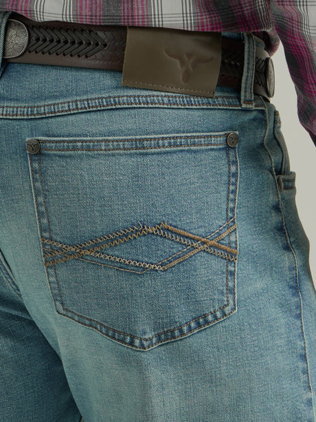 Close-up of an individual wearing Wrangler 20X Mens Light Wash Shade Bootcut Stretch Jeans - 112335407 with decorative back pocket stitching, paired with a black braided leather belt and a plaid shirt.