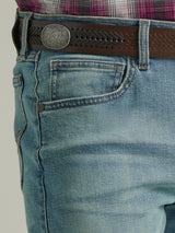 A close-up shows a person in Wrangler 20X Mens Light Wash Shade Bootcut Stretch Jeans (112335407) paired with a brown woven leather belt featuring a decorative round buckle, and a neatly tucked plaid shirt.