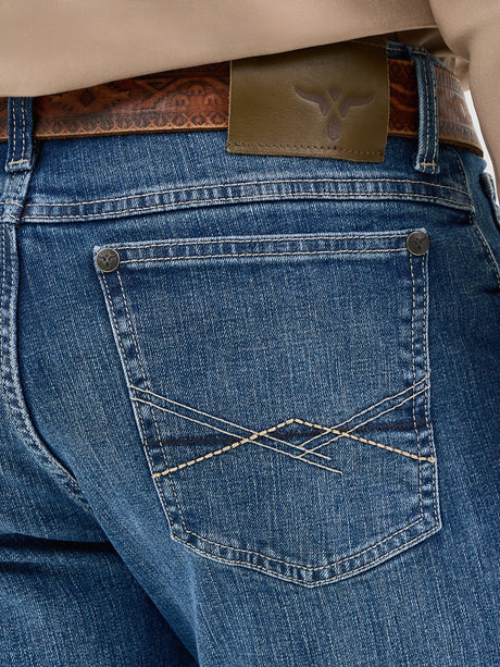 Close-up of a person wearing Mens Wrangler 20X No. 42 Vintage Bootcut Jeans, identifiable by their decorative stitching and Wrangler patch on the back pocket, secured with a brown patterned leather belt.