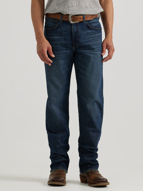 A person wearing a gray shirt, Wrangler 20X Sunnybrook Dark Wash Extreme Relaxed Straight Stretch Denim Jeans, a brown leather belt, and brown leather boots with a pointed toe stands against a plain background.