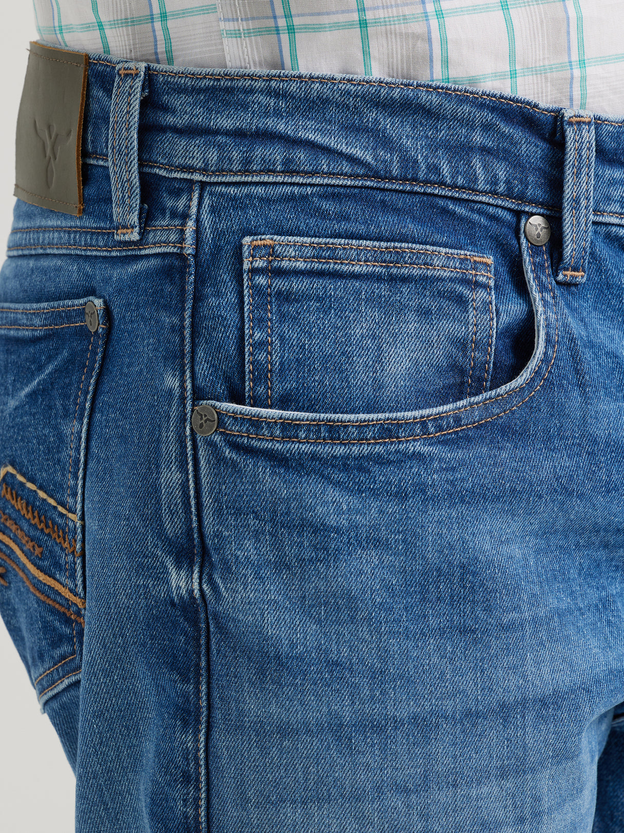 A person is wearing Wrangler 20x Mens Medium Wash Backwater Vintage Bootcut Stretch Denim Jeans, showcasing the small pocket and brown leather patch. Their plaid shirt with striped patterns pairs perfectly, adding a vintage denim vibe.