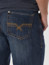 A person is seen in Wrangler® 20X® No. 33 Relaxed Straight Leg jeans, style 1033MWXWL, featuring dark blue denim and a back pocket with crossed orange stitching, complemented by the edge of a dark shirt at the waist.