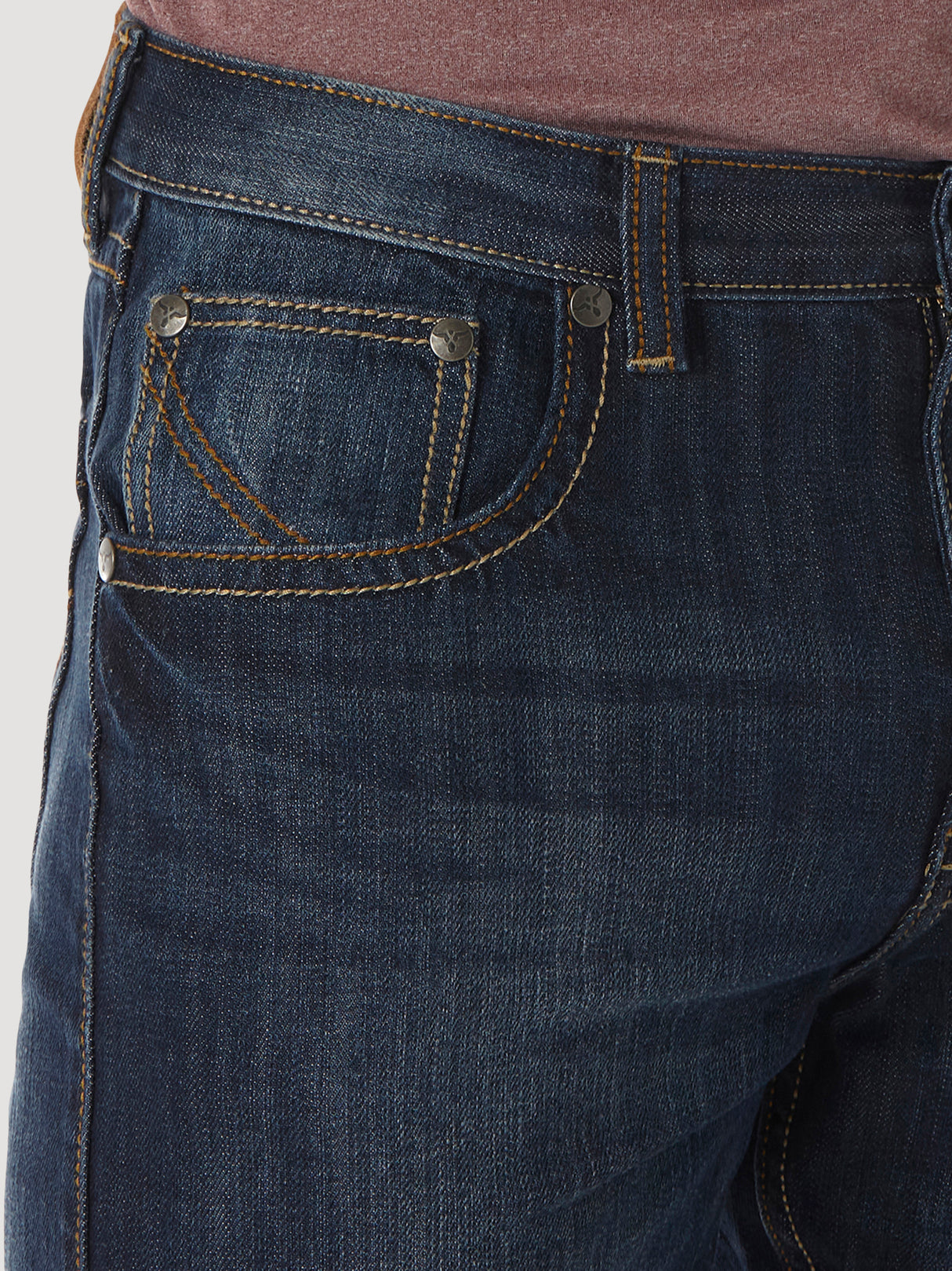 Close-up of a person wearing Wrangler® 20X® No. 42 - Vintage Boot Jean in dark blue denim with orange stitching and silver rivets, featuring front pocket detail, perfectly paired with a maroon top.