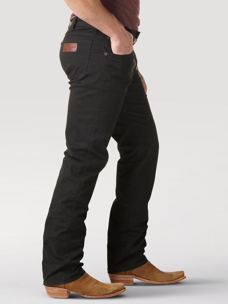 A person in a maroon shirt and Mens Wrangler Retro Slim Fit Straight Leg Pant - 88MWZBK with tan cowboy boots stands sideways, hand in pocket, against a light gray backdrop, highlighting the premium denims stylish appeal.