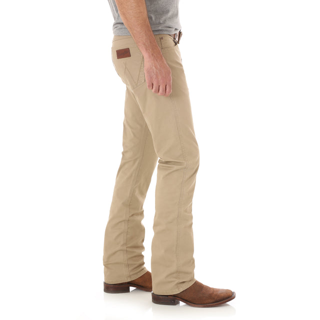 Wearing Mens Wrangler Retro Slim Fit Straight Leg Pants 1088MWZFN with a brown leather patch on the pocket, a gray shirt, and brown cowboy boots, they stand sideways against a white background, capturing the classic Wrangler Retro style.