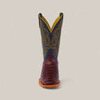 The Exotic Caiman Belly Tail boot in Wine features a square toe, brown crocodile-textured foot, dark upper shaft with intricate yellow stitching, showcased against a plain background for added flair.