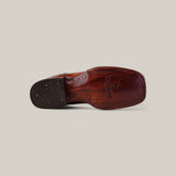 Bottom view of the Exotic American Alligator Hornback - Cogñac shoe on a light gray background, highlighting the textured sole and stitching. The embossed logo and text on the square toe sole evoke an exotic boots charm.