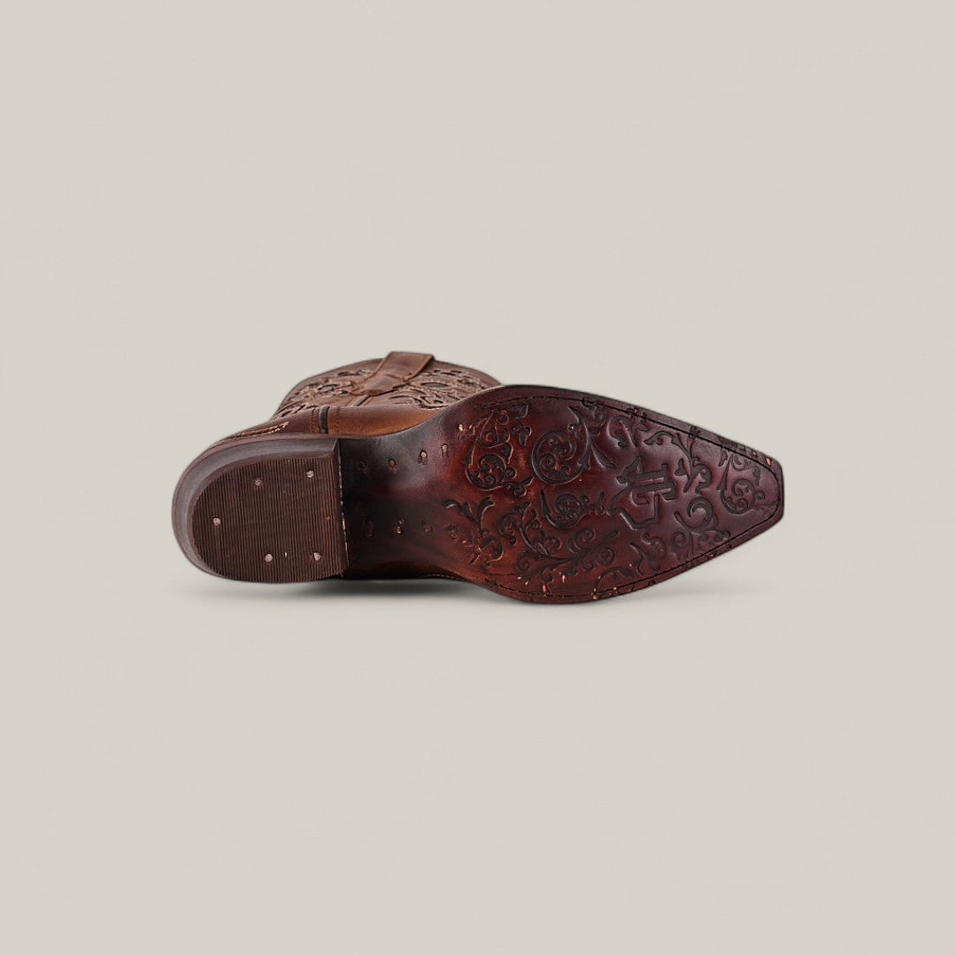 The Gina - Brown - Snip Toe boot is shown from the sole, displaying intricate floral patterns carved into brown leather and metal studs on the heel, set against a plain light background.