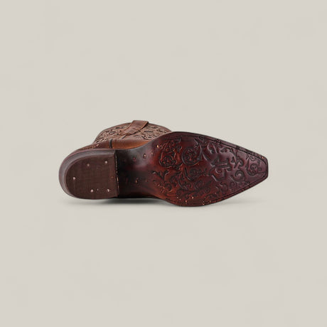 The Gina - Brown - Snip Toe boot is shown from the sole, displaying intricate floral patterns carved into brown leather and metal studs on the heel, set against a plain light background.