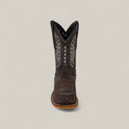 The Orion Suede Oxford - Square Toe Kids Boot is shown from the front in brown suede, featuring intricate white and silver stitching with decorative patterns, set against a plain light gray background.
