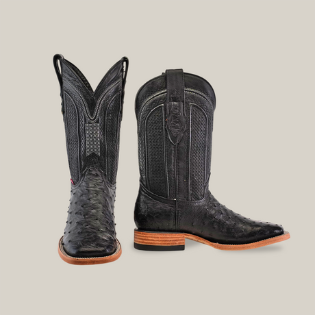 A pair of black Exotic Full Quilt Ostrich leather square toe cowboy boots with a wooden heel; one boot stands upright while the other shows its side profile, featuring classic stitching and pull straps for a unique touch.