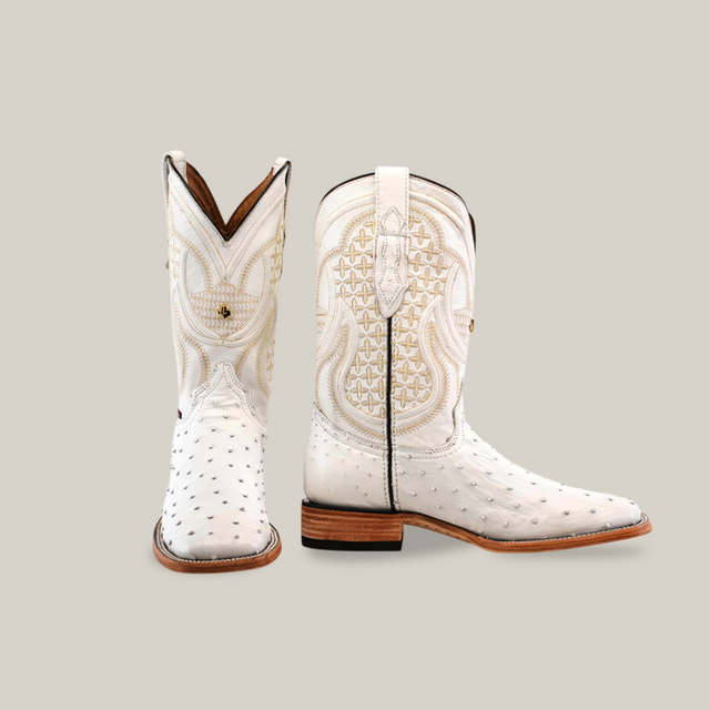 The Exotic Full Quilt Ostrich - White - Square Toe cowboy boots, crafted from exotic ostrich leather, have intricate stitching and a distinctive pattern. They feature a wooden sole and a top loop for easy pull-on, with one boot facing forward and the other side-on.