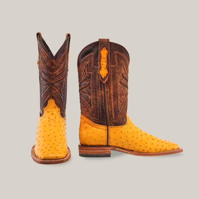 The Exotic Full Quilt Ostrich - Buttercup- Square Toe features textured buttercup ostrich leather on the lower half, paired with a dark brown upper adorned with intricate stitching, all set against a light gray background for added rustic charm.